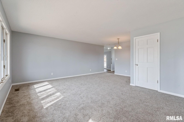 spare room featuring carpet flooring, a notable chandelier, visible vents, and baseboards