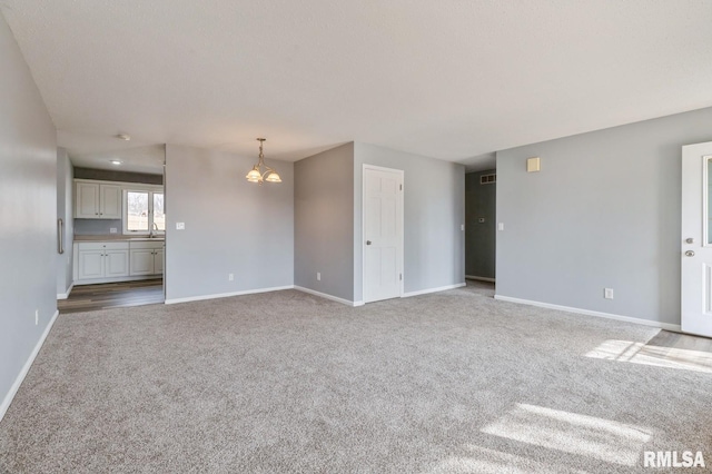 unfurnished living room with carpet floors, baseboards, and a notable chandelier