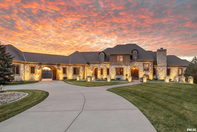 french country inspired facade with a chimney, curved driveway, and a lawn