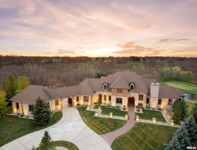 french country style house featuring stone siding, a front lawn, and concrete driveway