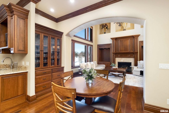 dining room with arched walkways, crown molding, dark wood finished floors, a high end fireplace, and baseboards