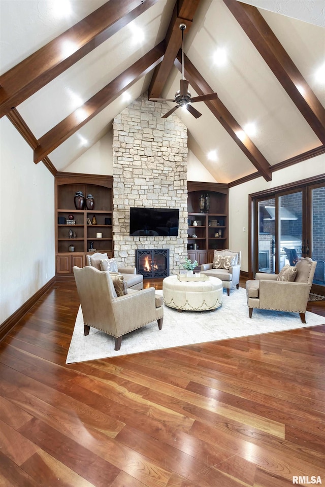 living room featuring ceiling fan, a stone fireplace, beamed ceiling, and wood finished floors