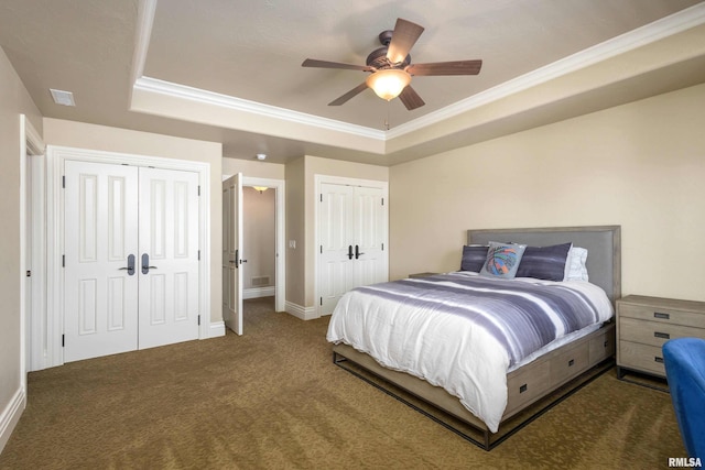 carpeted bedroom with ceiling fan, two closets, baseboards, a raised ceiling, and crown molding