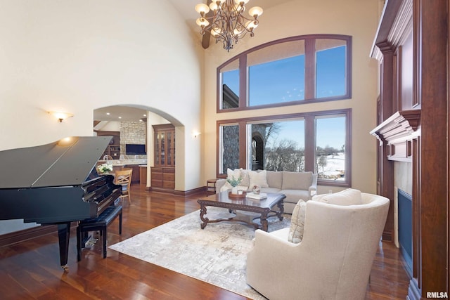 living area with arched walkways, a chandelier, a high ceiling, baseboards, and dark wood finished floors