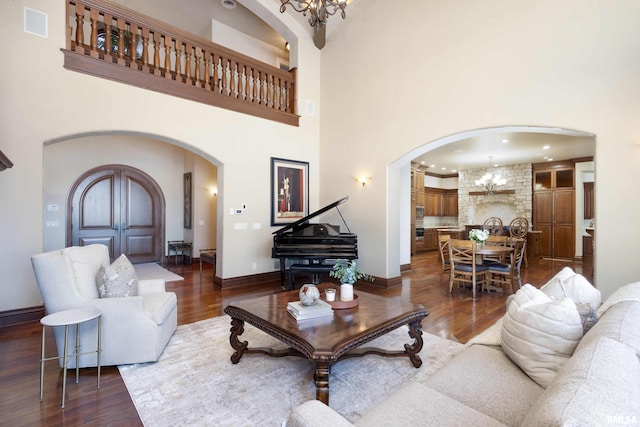 living area featuring dark wood-type flooring, arched walkways, baseboards, and an inviting chandelier