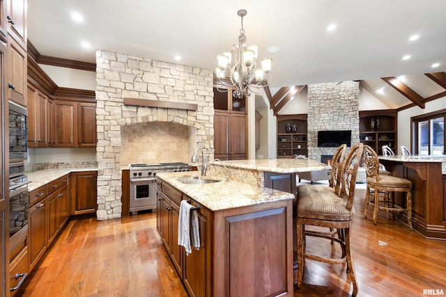 kitchen with a center island with sink, high end stainless steel range oven, light wood-style floors, a kitchen bar, and a sink