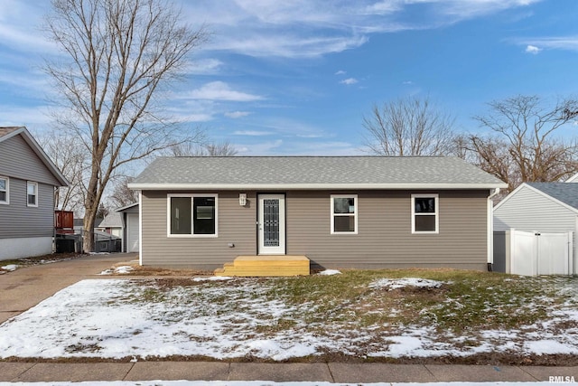 ranch-style house featuring central AC unit, fence, and roof with shingles