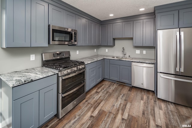 kitchen featuring appliances with stainless steel finishes, dark wood-type flooring, a textured ceiling, gray cabinetry, and a sink