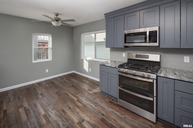 kitchen with baseboards, appliances with stainless steel finishes, dark wood-type flooring, gray cabinets, and a textured ceiling