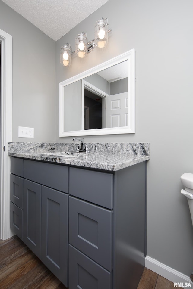 bathroom with baseboards, toilet, wood finished floors, a textured ceiling, and vanity