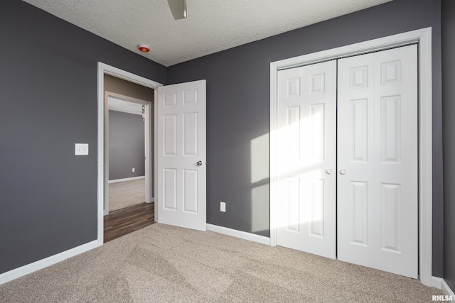 unfurnished bedroom with a textured ceiling, carpet floors, a closet, and baseboards