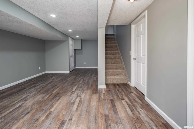 finished basement featuring baseboards, dark wood-style flooring, stairs, a textured ceiling, and recessed lighting