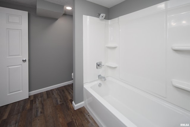 bathroom with tub / shower combination, toilet, baseboards, and wood finished floors