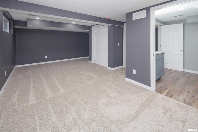 finished below grade area with carpet, baseboards, visible vents, and a textured ceiling