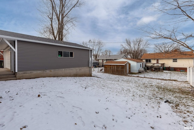 snow covered rear of property with a garage, a storage shed, and an outbuilding