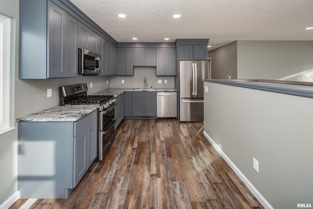 kitchen featuring light stone counters, dark wood-style floors, gray cabinetry, appliances with stainless steel finishes, and a sink