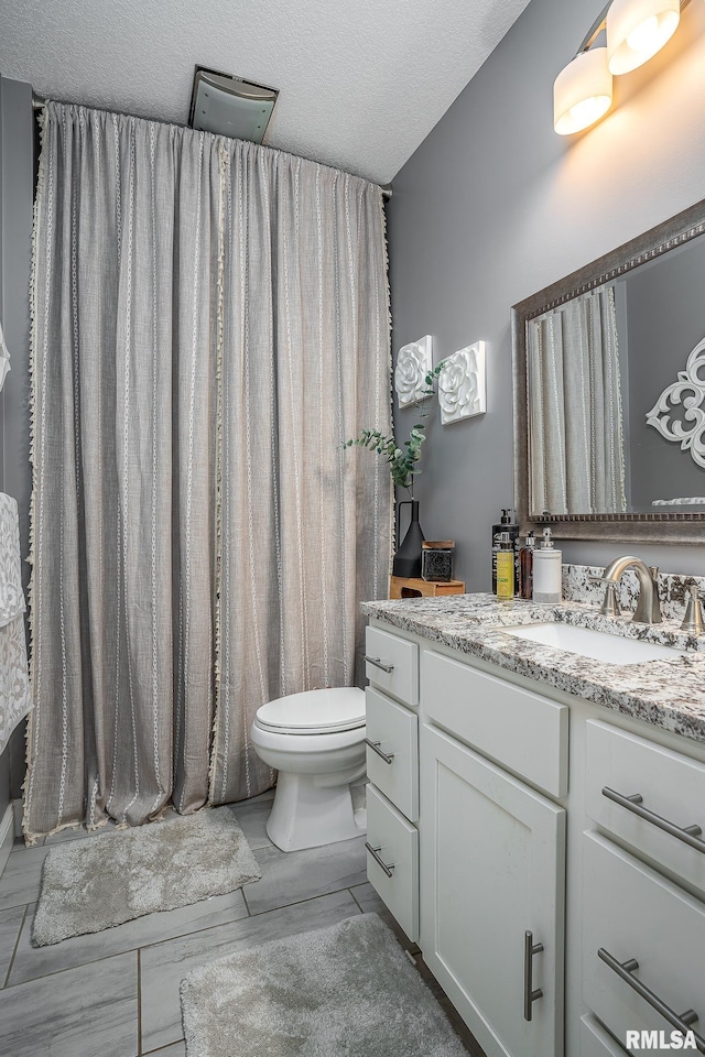 bathroom with toilet, a textured ceiling, and vanity