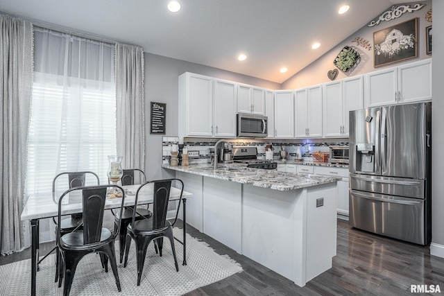 kitchen with light stone counters, stainless steel appliances, lofted ceiling, decorative backsplash, and a peninsula