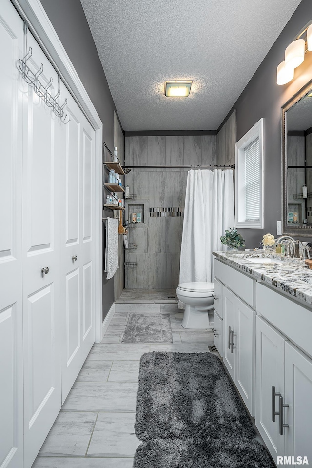 bathroom featuring a textured ceiling, vanity, a tile shower, and toilet