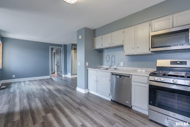 kitchen featuring stainless steel appliances, light countertops, a sink, wood finished floors, and baseboards