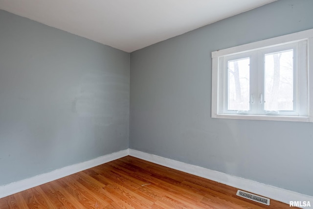 spare room featuring wood finished floors, visible vents, and baseboards