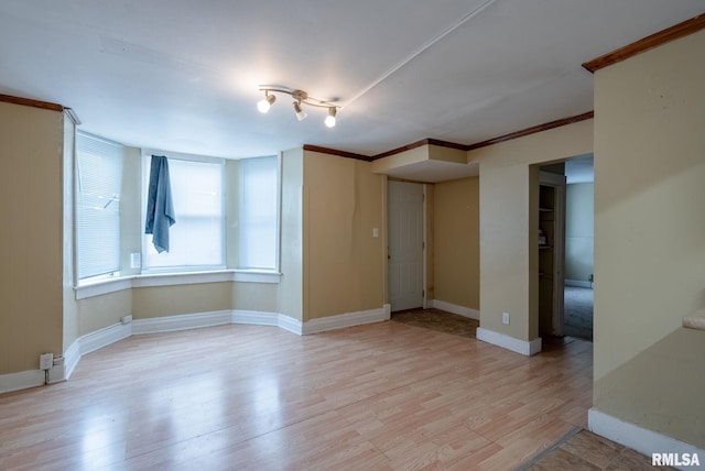 spare room featuring baseboards, light wood finished floors, and crown molding