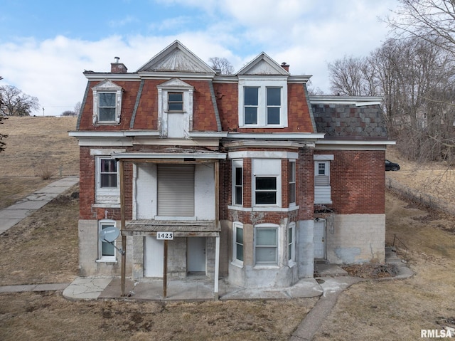 view of front facade featuring a chimney, mansard roof, and brick siding