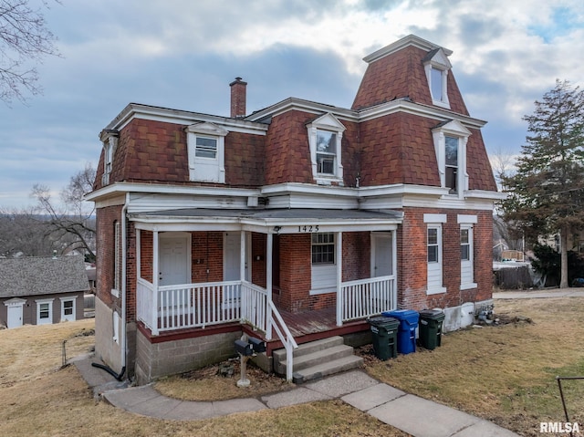 second empire-style home with a porch, a chimney, mansard roof, and brick siding