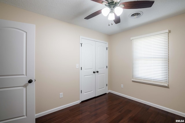 unfurnished bedroom with baseboards, visible vents, dark wood-type flooring, a textured ceiling, and a closet