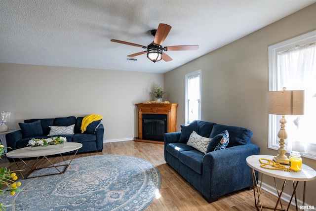 living room featuring a textured ceiling, plenty of natural light, a fireplace, and wood finished floors