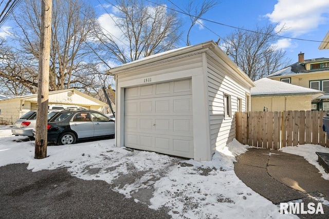 snow covered garage featuring fence and a detached garage