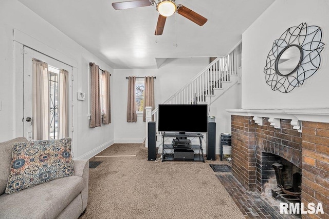 carpeted living room featuring a ceiling fan, a fireplace, baseboards, and stairs