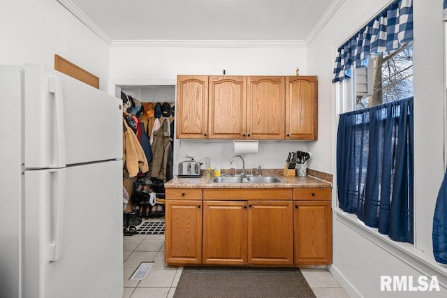 kitchen with light tile patterned floors, a sink, freestanding refrigerator, brown cabinetry, and crown molding