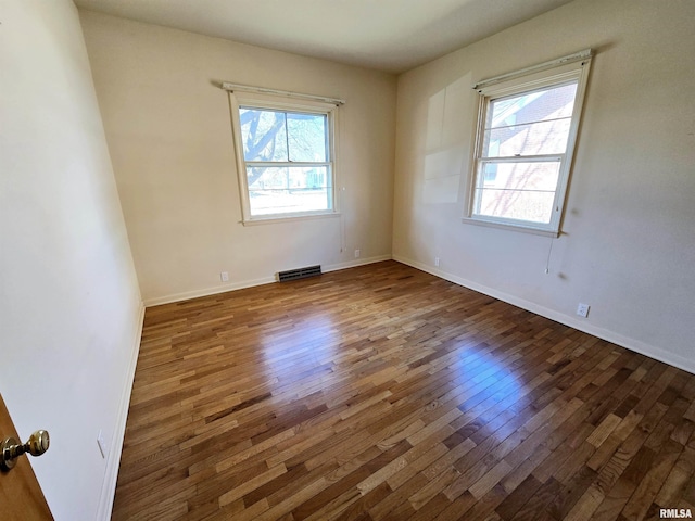 spare room with plenty of natural light, wood-type flooring, visible vents, and baseboards