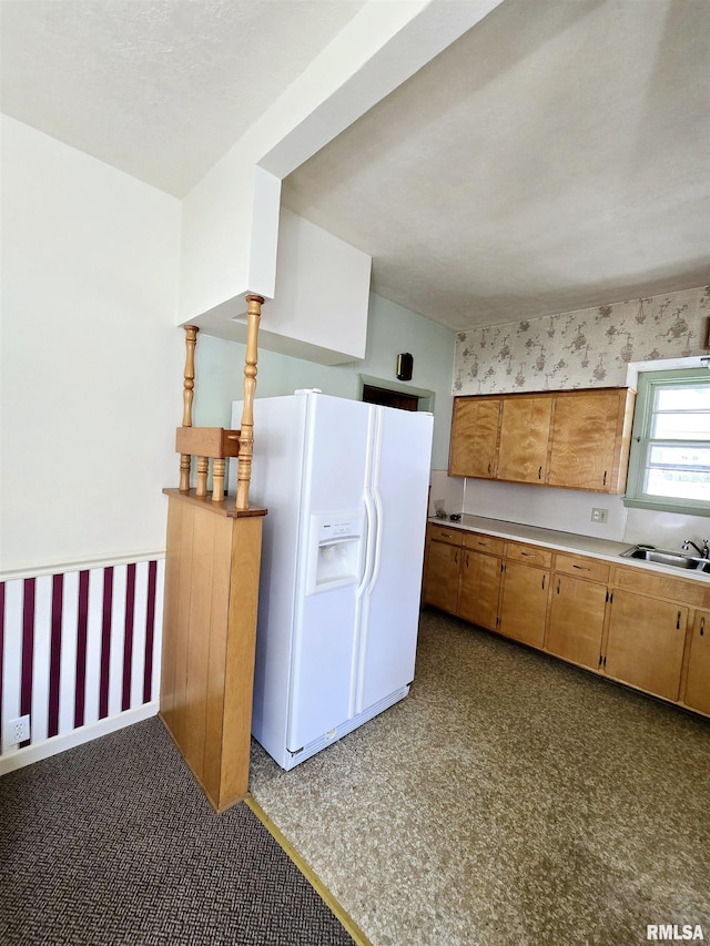 kitchen with brown cabinets, light countertops, a sink, white fridge with ice dispenser, and wallpapered walls