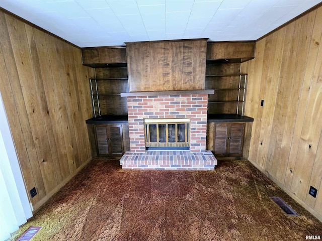 unfurnished living room featuring built in shelves, a fireplace, visible vents, carpet flooring, and wood walls