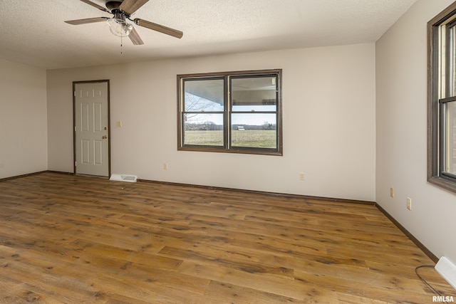 empty room featuring hardwood / wood-style flooring, a ceiling fan, visible vents, and a textured ceiling