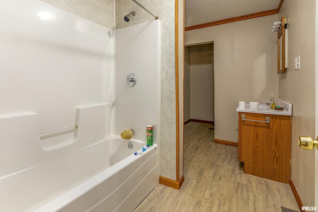 full bath featuring baseboards, ornamental molding, wood finished floors,  shower combination, and vanity