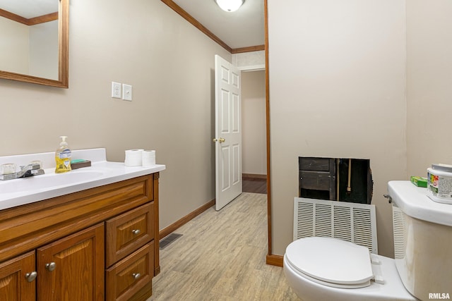 half bathroom featuring visible vents, toilet, ornamental molding, wood finished floors, and vanity