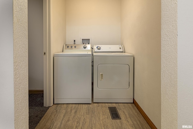 clothes washing area with wood finished floors, washing machine and dryer, visible vents, and baseboards