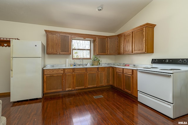 kitchen featuring white appliances, a sink, vaulted ceiling, light countertops, and dark wood finished floors