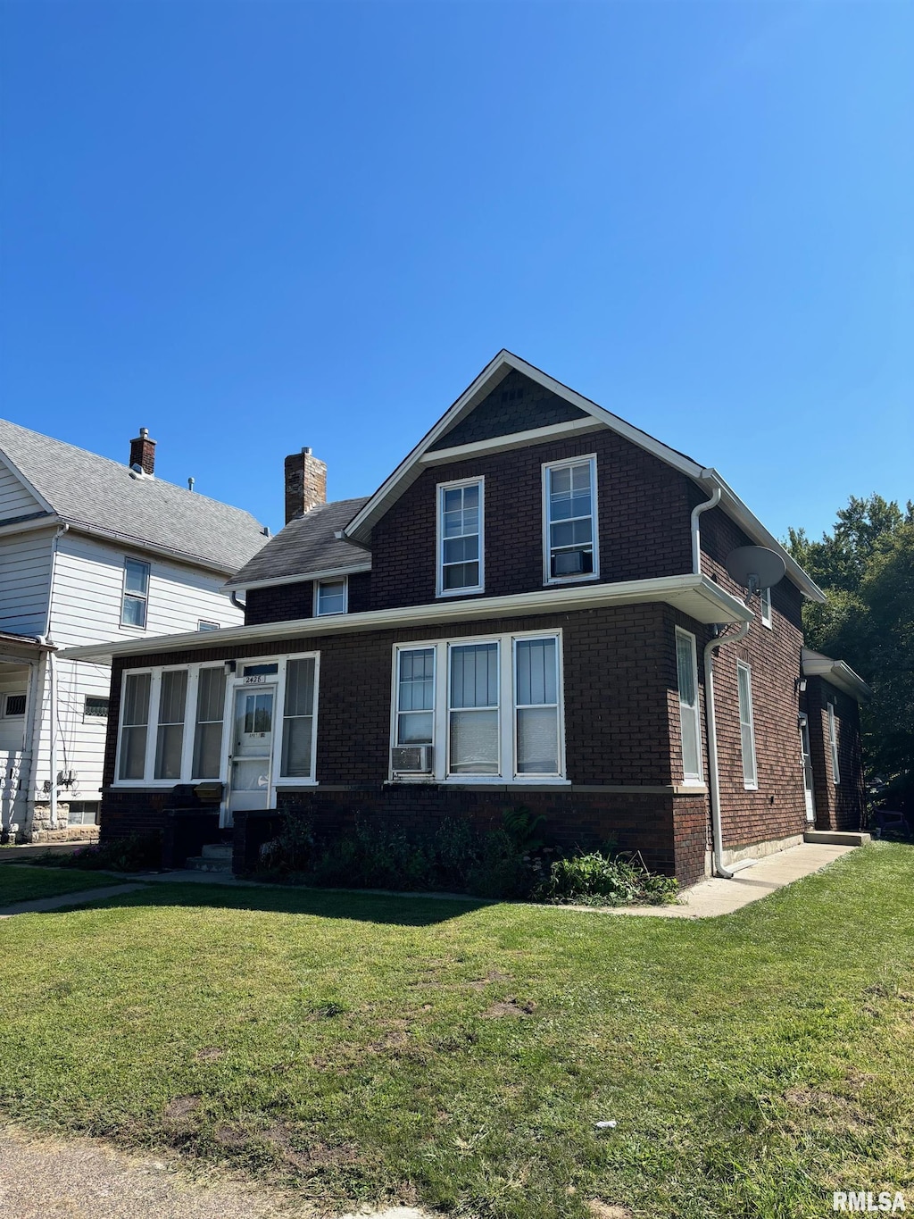 view of front of home with cooling unit, brick siding, a sunroom, a chimney, and a front yard