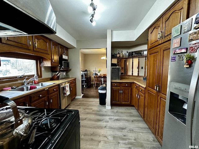 kitchen with light wood finished floors, stainless steel appliances, light countertops, a sink, and extractor fan