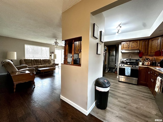 kitchen featuring dark wood-style floors, a textured ceiling, stainless steel gas range, under cabinet range hood, and baseboards