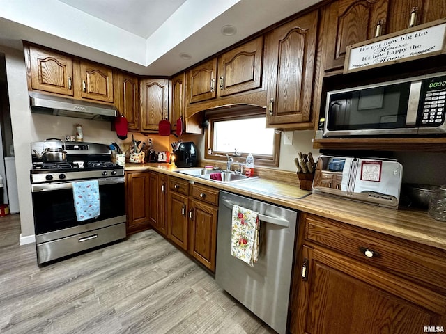 kitchen with stainless steel appliances, light countertops, light wood-style floors, a sink, and under cabinet range hood