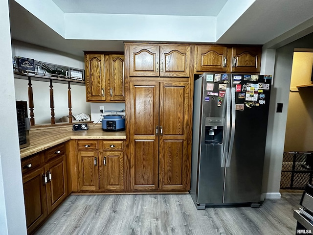 kitchen with light wood finished floors, stainless steel refrigerator with ice dispenser, light countertops, and brown cabinetry