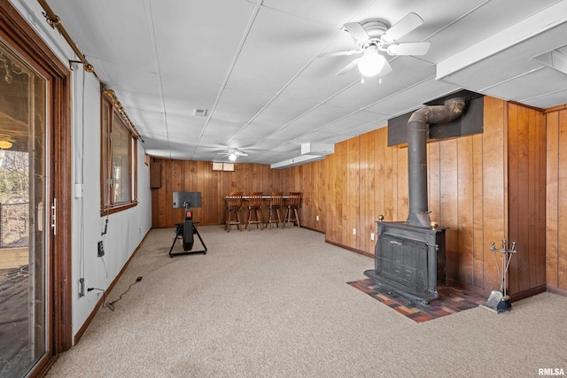 below grade area with carpet, visible vents, a wood stove, wooden walls, and a bar