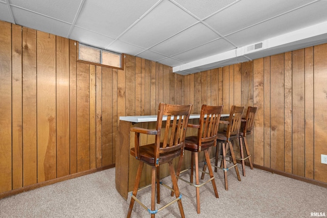 dining room featuring a bar, wooden walls, and light carpet