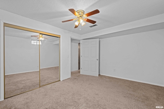 unfurnished bedroom with a textured ceiling, carpet flooring, visible vents, a ceiling fan, and a closet