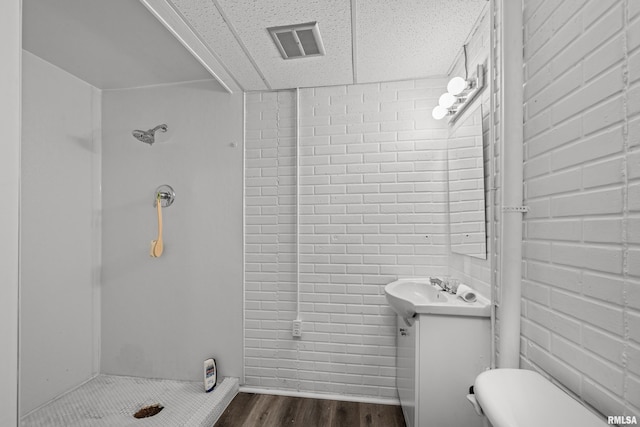 full bathroom featuring visible vents, vanity, brick wall, wood finished floors, and walk in shower